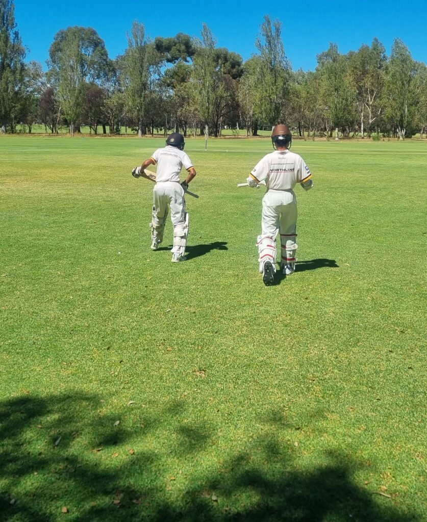 Two boy running on to a cricket field from the sidelines, captured from behind.